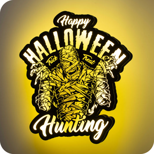 image of a 3d wall mounted acrylic light, backlit by yellow multicolor lights, featuring a cartoon style scary halloween themed illustration. A scary Egyptian mummy sits front and centre. Above the mummy illustration sits some spooky halloween themed text that reads "happy halloween" "trick" "treat". Below the mummy sits some more halloween themed text that reads "hunting".