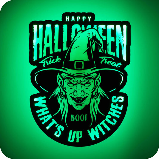 a 3d wall mounted acrylic light, backlit by green multi-colour led lights, featuring a cartoon style scary halloween themed illustration. A cunning witches head commands the centre of the light, her evil grin and drooping hat will send chills down your spine. Above her hat sits some spooky halloween themed text that reads "happy halloween" "trick" "treat". Below her long pointy chin, the light is complete with further text that reads "boo!" and "what's up witches" adding a light hearted twist to the light.