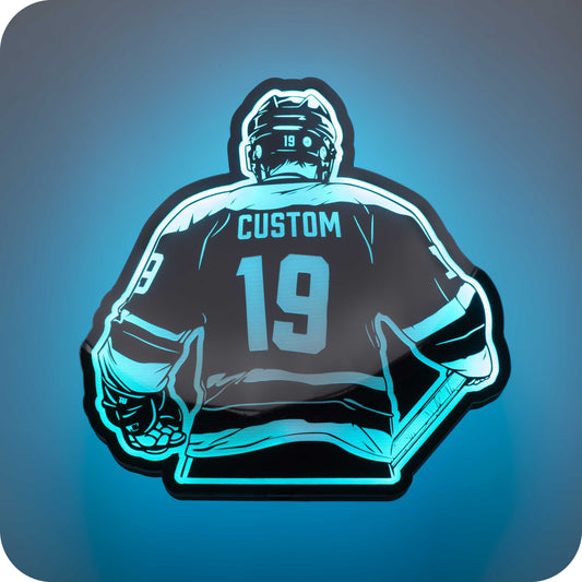 a 3d wall mounted acrylic light, back-lit by  multi-color led lights, featuring a cartoon style illustration of an ice hockey player holding his hockey stick, view from behind showing the back of the ice hockey players players jersey. The text and number on the back of the jersey can be personalised.